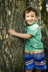 Porträt eines lächelnden kaukasischen Jungen, der einen Baum umarmt - BLEF02867