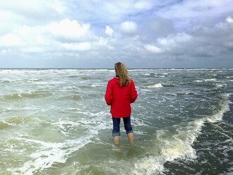 Belgien, Flandern, Nordsee, Frau steht barfuß in den Wellen des Meeres und entspannt sich - GWF06070
