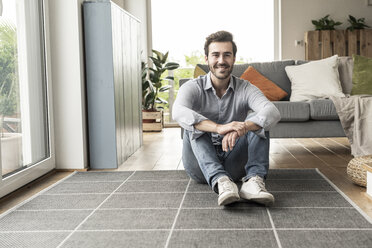 Confident young man sitting on floor of his livingroom - UUF17311