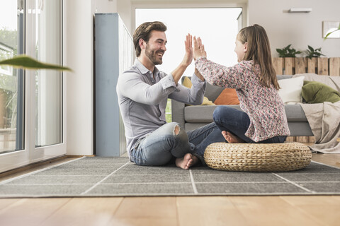 Junger Mann und kleines Mädchen sitzen zu Hause und geben sich die Hand, lizenzfreies Stockfoto