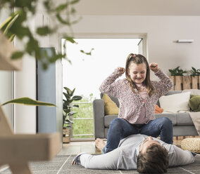 Young man and little girl having a pillow fight in the living room - UUF17326