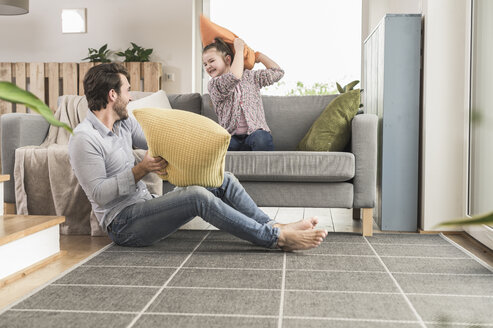 Junger Mann und kleines Mädchen bei einer Kissenschlacht im Wohnzimmer - UUF17328