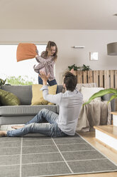 Young man and little girl having a pillow fight in the living room - UUF17330