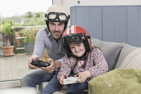 Junger Mann und kleines Mädchen tragen Motorradhelme und spielen ein Rennspiel mit Spielkonsolen - UUF17340