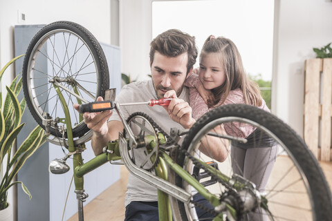 Junger Mann und kleines Mädchen reparieren gemeinsam ein Fahrrad, lizenzfreies Stockfoto