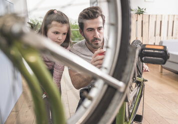 Young man and little girl repairing bicycle together - UUF17368
