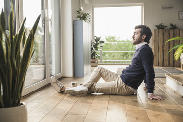 Young man sitting on floor, looking out of window, relaxing - UUF17385