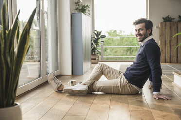 Young man sitting on floor, looking out of window, relaxing - UUF17386
