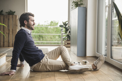 Junger Mann sitzt auf dem Boden, schaut aus dem Fenster und entspannt sich - UUF17387