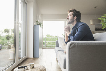 Junger Mann sitzt zu Hause auf der Couch und schaut aus dem Fenster - UUF17408