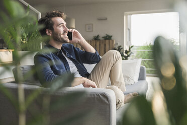 Junger Mann sitzt zu Hause auf der Couch und benutzt sein Smartphone - UUF17412