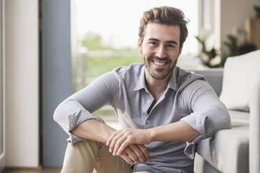 Portrait of young man sitting in his livingroom - UUF17426