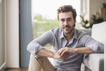 Portrait of young man sitting in his livingroom - UUF17427