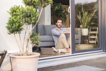 Young man relaxing in his comfortable home, looking out of window - UUF17434