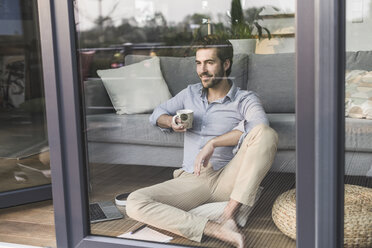 Junger Mann sitzt vor einem Fenster und trinkt Kaffee - UUF17435