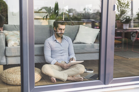 Junger Mann sitzt auf dem Boden vor einem Fenster und macht sich Notizen, lizenzfreies Stockfoto