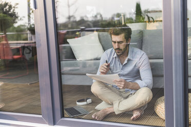 Young man sitting on ground, in front of window, taking notes - UUF17437