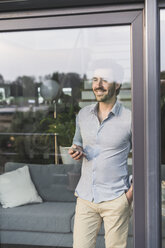 Junger Mann schaut aus dem Fenster und benutzt sein Smartphone - UUF17439