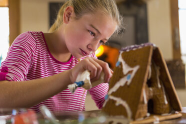 Caucasian girl spreading icing on gingerbread house - BLEF02918