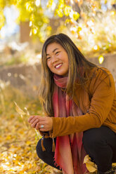 Smiling Asian woman holding leaf in autumn - BLEF02919