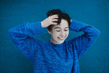 Lächelnde kaukasische Frau mit zerzausten Haaren in der Nähe einer blauen Wand - BLEF02978