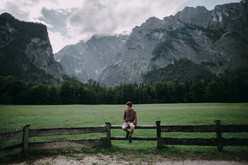 Caucasian man sitting on wooden fence near mountains - BLEF02988