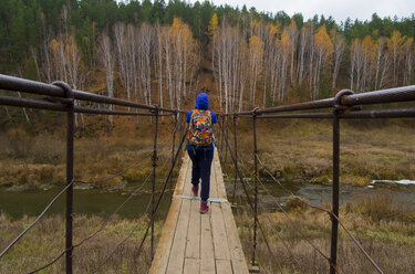 Caucasian woman crossing river on wooden footbridge - BLEF03039