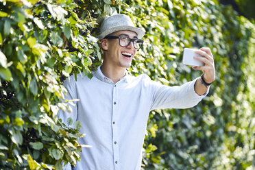 Glücklicher junger Mann macht Selfie in einer Hecke - BSZF01064