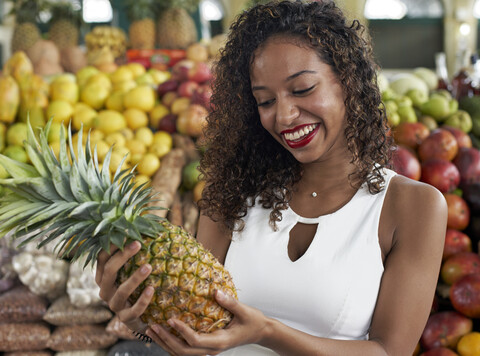 Porträt einer lächelnden Frau mit Ananas in der Markthalle, lizenzfreies Stockfoto