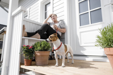 Entspannte ältere Frau sitzt mit ihrem Hund auf der Veranda - KMKF00913