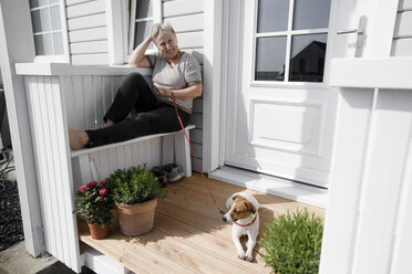 Entspannte ältere Frau sitzt mit ihrem Hund auf der Veranda - KMKF00914