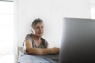 Ältere Frau sitzt zu Hause am Tisch und benutzt einen Laptop - KMKF00920