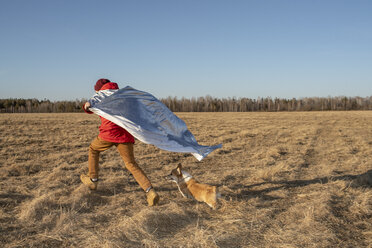 Boy dressed up as superhero running with dog in steppe landscape - VPIF01226