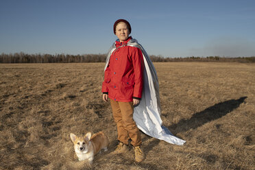 Boy dressed up as superhero standing with dog in steppe landscape - VPIF01228