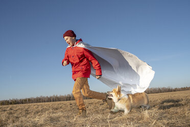 Boy dressed up as superhero running with dog in steppe landscape - VPIF01232