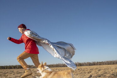 Boy dressed up as superhero running with dog in steppe landscape - VPIF01233