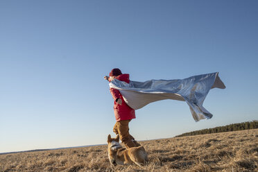 Boy dressed up as superhero running with dog in steppe landscape - VPIF01234