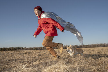 Boy dressed up as superhero running with dog in steppe landscape - VPIF01235