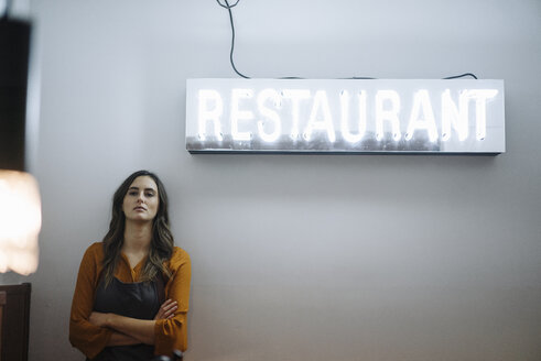 Ernste junge Frau lehnt an einer Wand unter Restaurant Neonlicht - KNSF05741