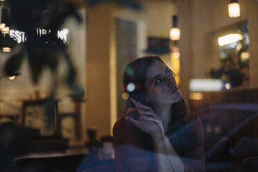 Ernste junge Frau sitzt am Tisch in einem Restaurant und schaut weg - KNSF05744