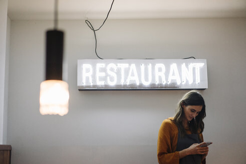 Junge Frau benutzt Handy unter Neonlicht im Restaurant - KNSF05753