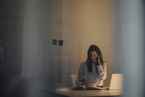 Junge Geschäftsfrau arbeitet spät am Schreibtisch im Büro, lizenzfreies Stockfoto