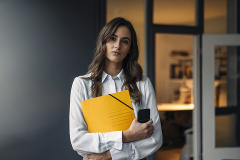 Portrait of serious young businesswoman holding folder and cell phone stock photo