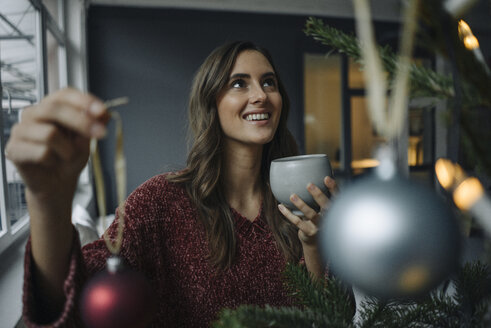 Lächelnde junge Frau beim Schmücken des Weihnachtsbaums - KNSF05804