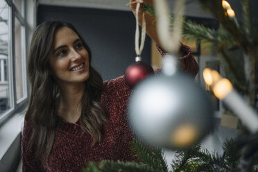 Lächelnde junge Frau beim Schmücken des Weihnachtsbaums - KNSF05805