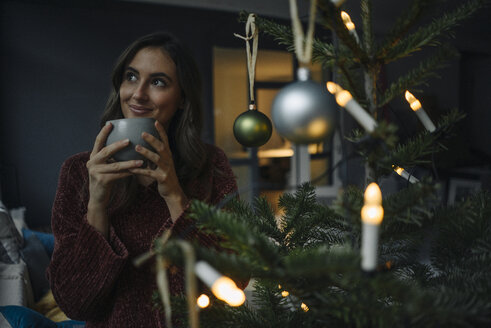 Junge Frau am geschmückten Weihnachtsbaum mit Tasse - KNSF05807