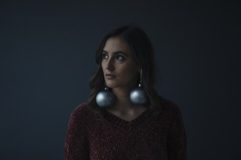 Porträt einer jungen Frau, die Weihnachtskugeln als Ohrringe trägt, lizenzfreies Stockfoto