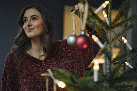 Young woman decorating Christmas tree looking away stock photo