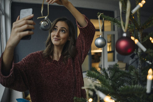Lächelnde junge Frau macht ein Selfie am Weihnachtsbaum - KNSF05813