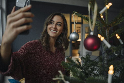 Lächelnde junge Frau macht ein Selfie am Weihnachtsbaum - KNSF05814